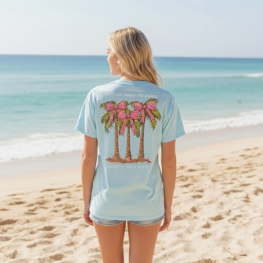 Woman on a beach wearing a light blue t-shirt with palm tree design.