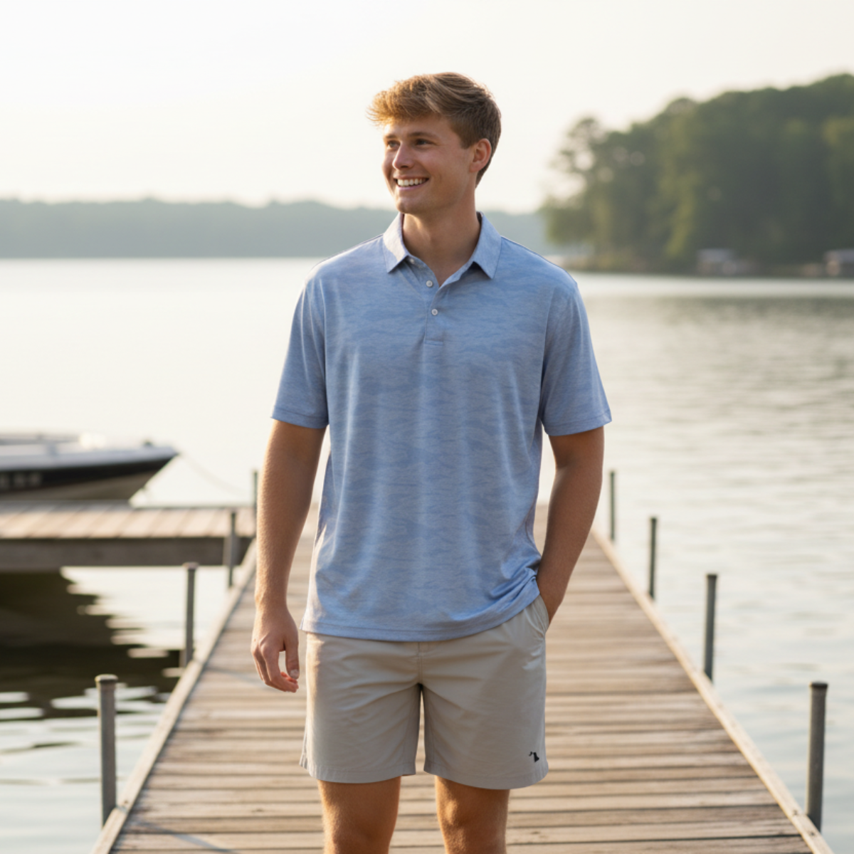 Man standing on a dock by a lake wearing a blue polo shirt and beige shorts.