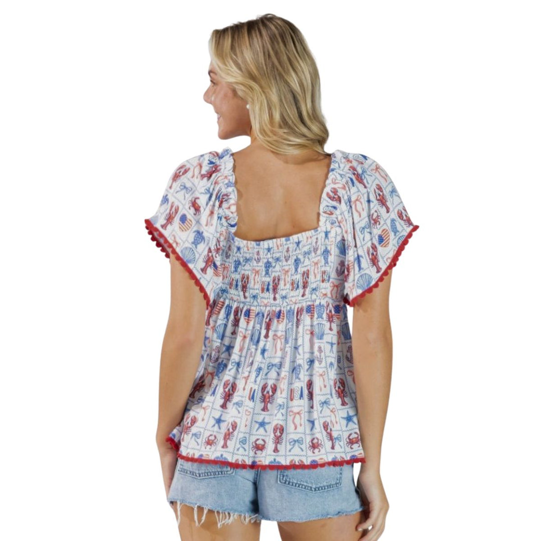 Back of woman wearing a patterned patriotic top and denim shorts on a white background