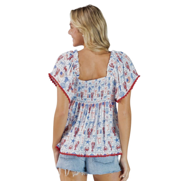 Back of woman wearing a patterned patriotic top and denim shorts on a white background