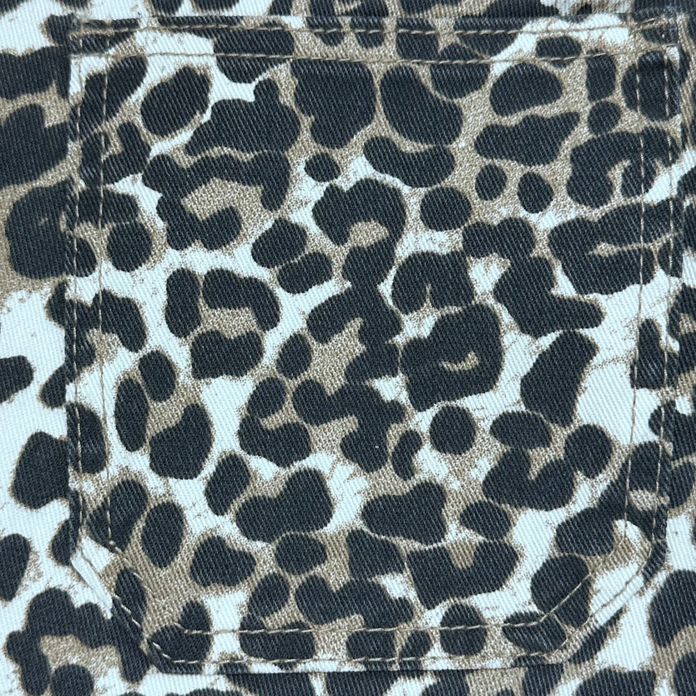 Close-up of a leopard print fabric with a stitched pocket, featuring black and dark brown spots on a light beige background.