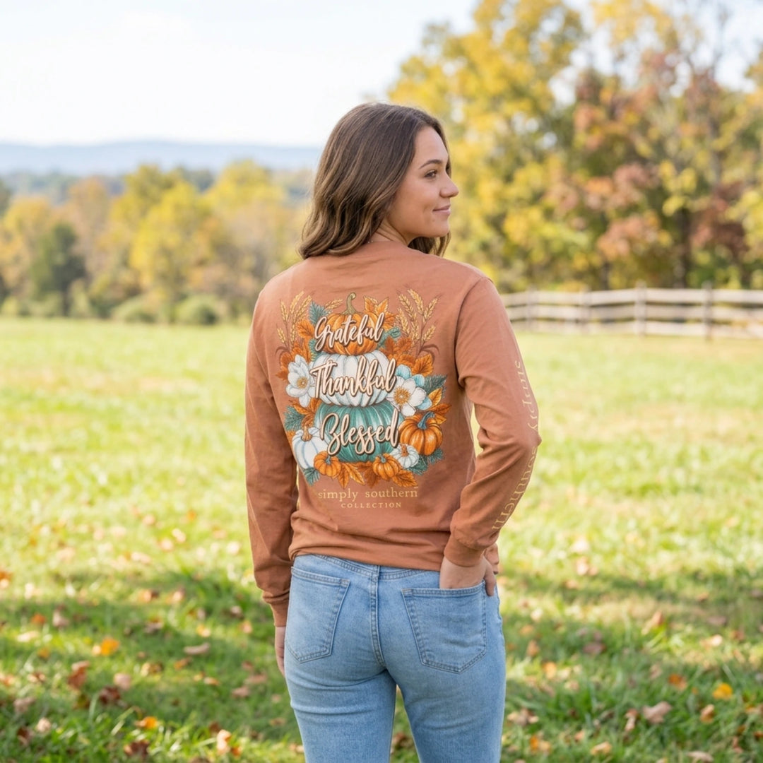 Woman wearing a Simply Southern fall graphic long sleeve tee with pumpkins and floral artwork in an autumn outdoor setting.